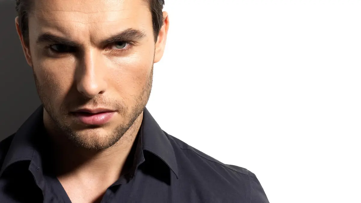 Fashion portrait of young man in black shirt poses over wall with contrast shadows