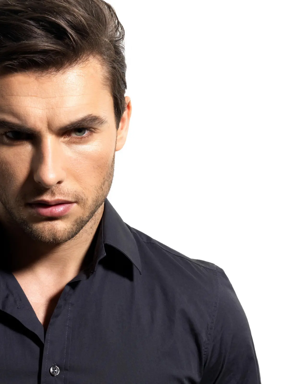 Fashion portrait of young man in black shirt poses over wall with contrast shadows