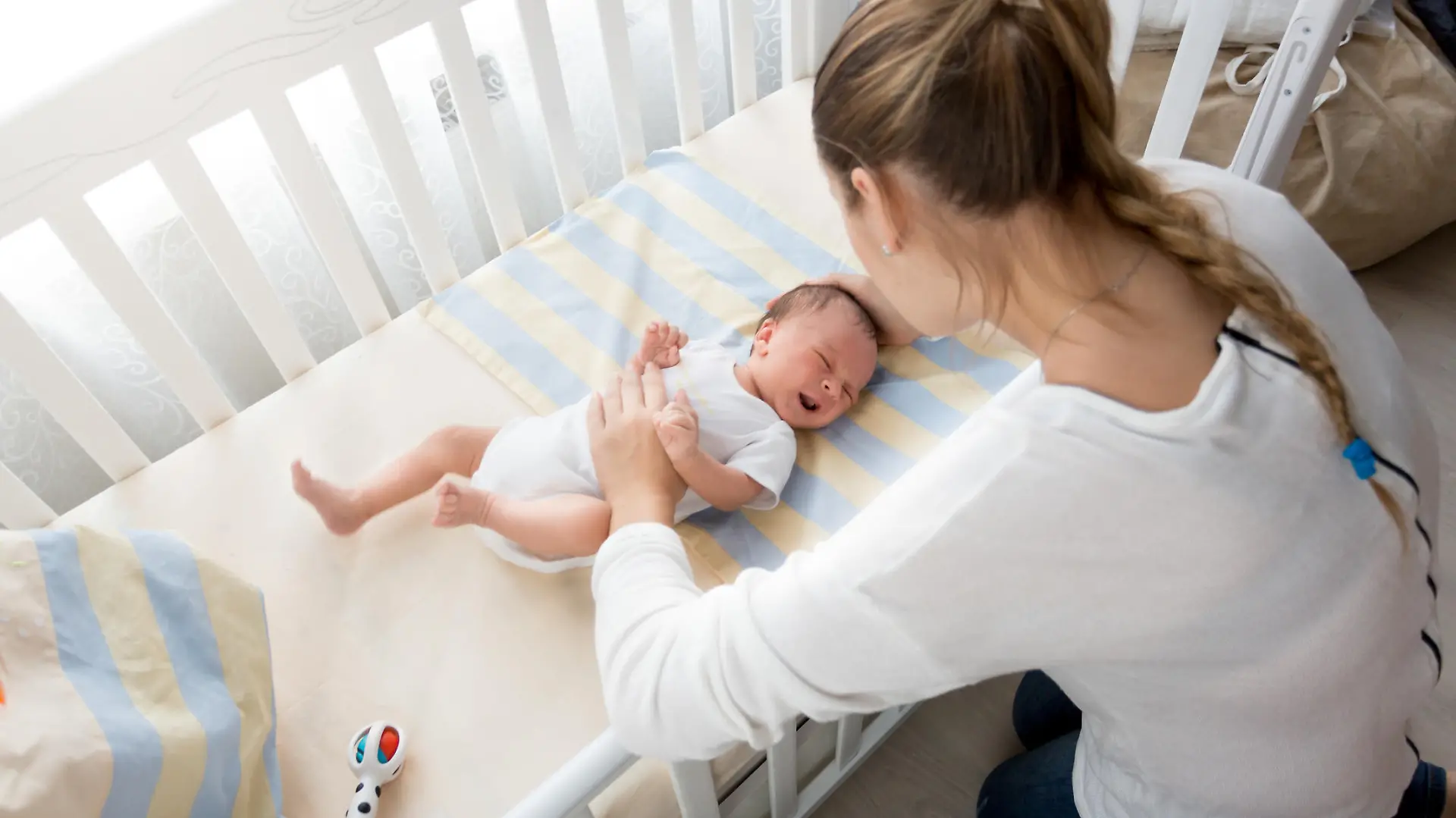 Young mother sitting near the cradle and holding baby's hand