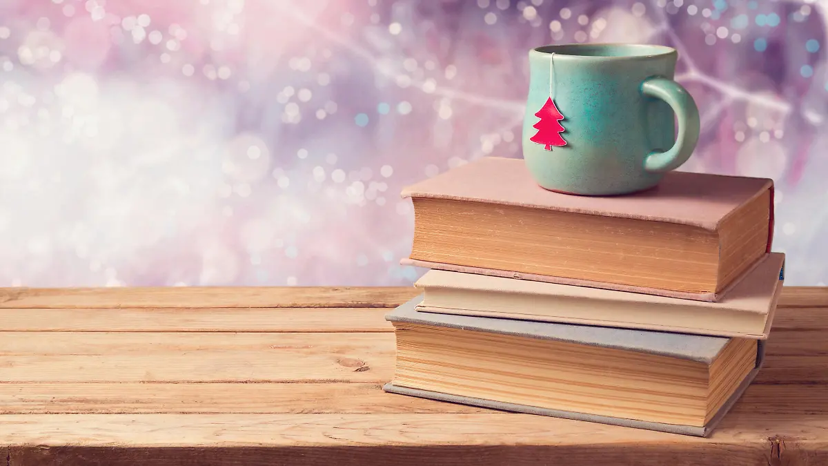 Christmas cup of tea and vintage books on wooden table over beautiful winter bokeh background with copy space