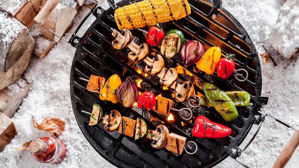 Overhead view of colorful vegetable kebabs and a corncob grilling on a winter BBQ outdoors in snow with tasty spicy dips and the wood pile alongside PUBLICATIONxINxGERxSUIxAUTxONLY Copyright: xfoodandmorex Panthermedia15952217  