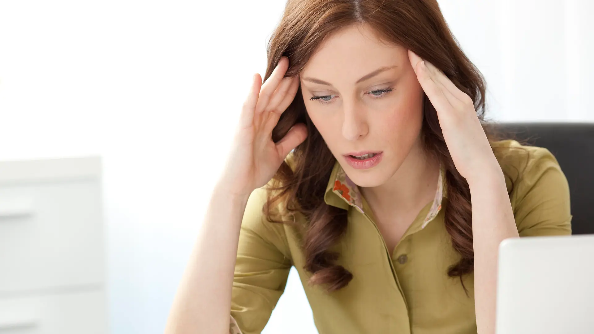 "Young Businesswoman Having Headache in the office, doing massage of the head and sitting at the desk."