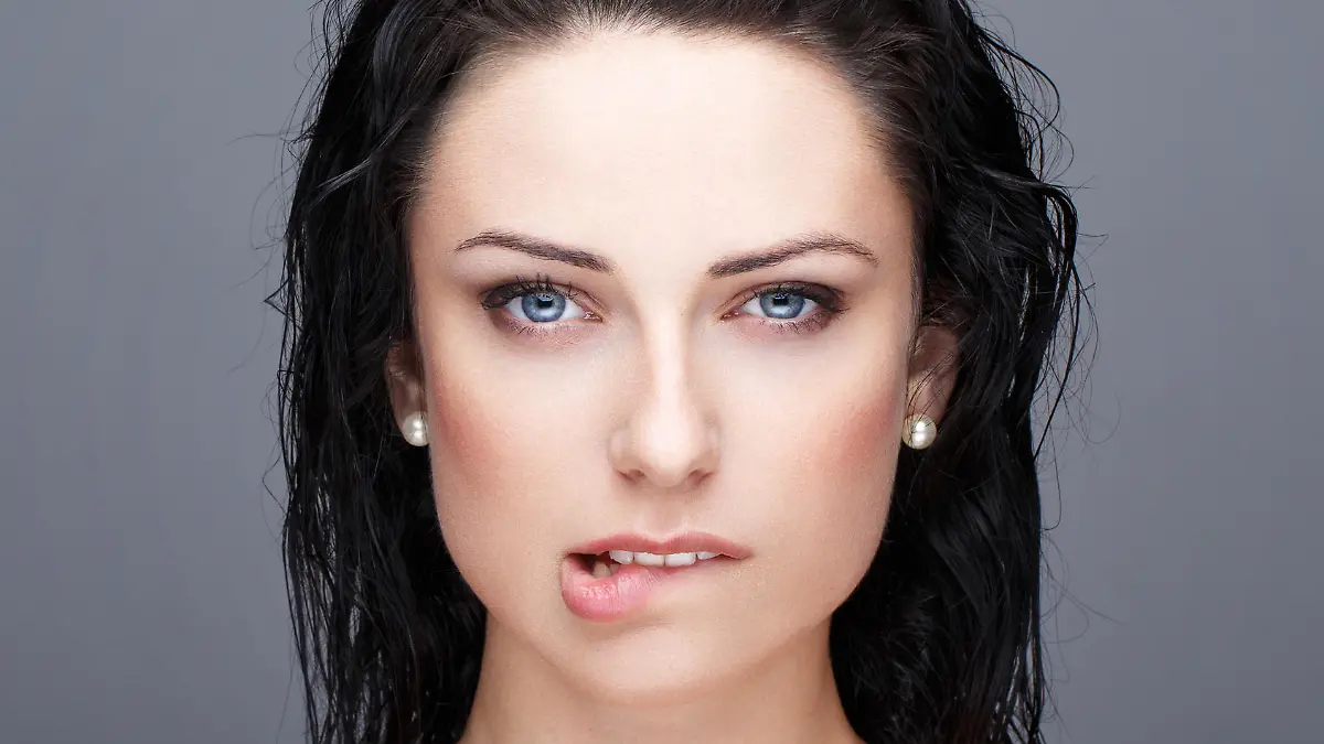 Sexy brunette woman bite lips portrait on grey