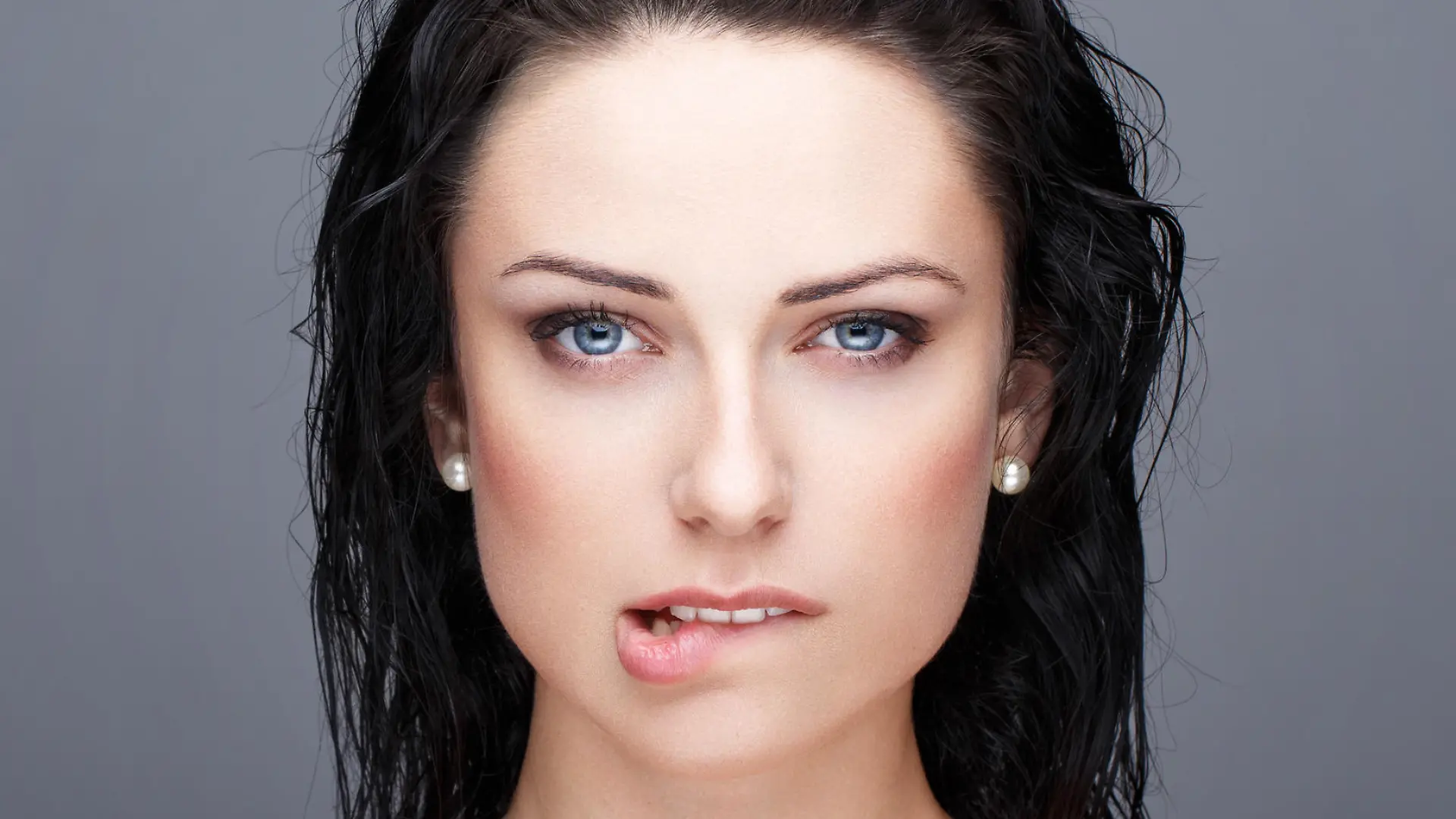 Sexy brunette woman bite lips portrait on grey