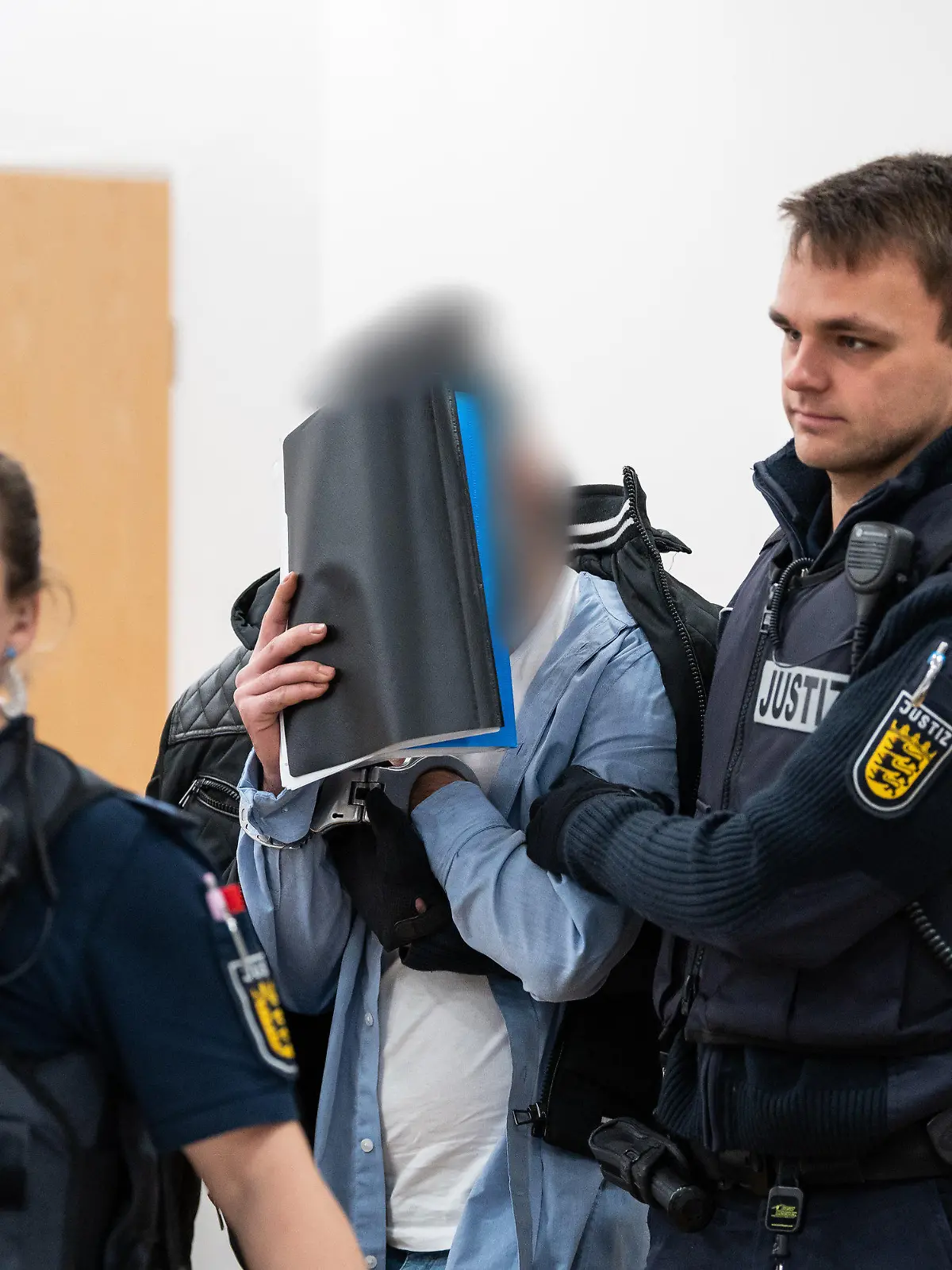 26.01.2023, Baden-Württemberg, Konstanz: Ein Mann (M), der wegen Vergewaltigung und Freiheitsberaubung an seiner Schwester angeklagt ist, verdeckt sein Gesicht, während er von Justiz Beamten in den Gerichtssaal geführt wird. Der Angeklagten soll seine, zur Tatzeit 18-jährige, Schwester in seinem WG-Zimmer in Konstanz eingesperrt, verletzt und mehrmals vergewaltigt haben. Foto: Silas Stein/dpa +++ dpa-Bildfunk +++