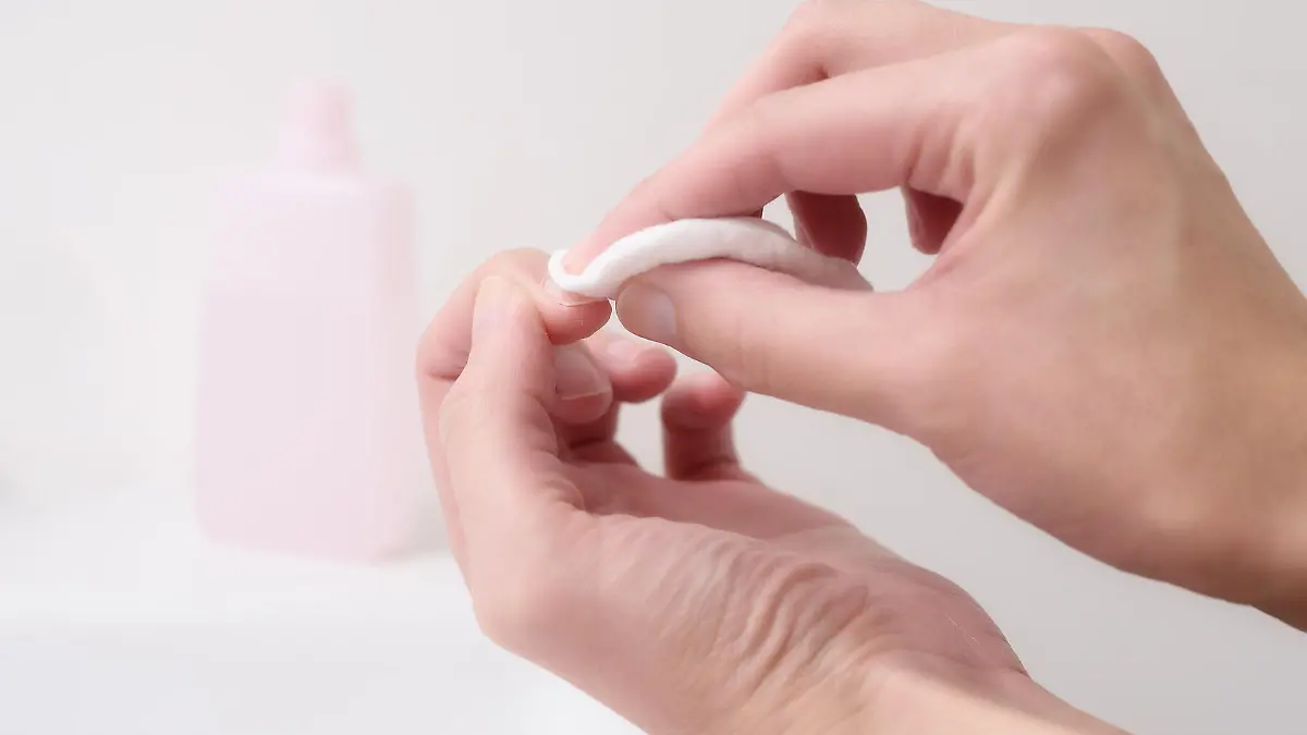 Woman removing nail varnish with acetone on a small cotton pad on the edge of a hand basin as she cares for her nails and cuticles in a health and beauty concept