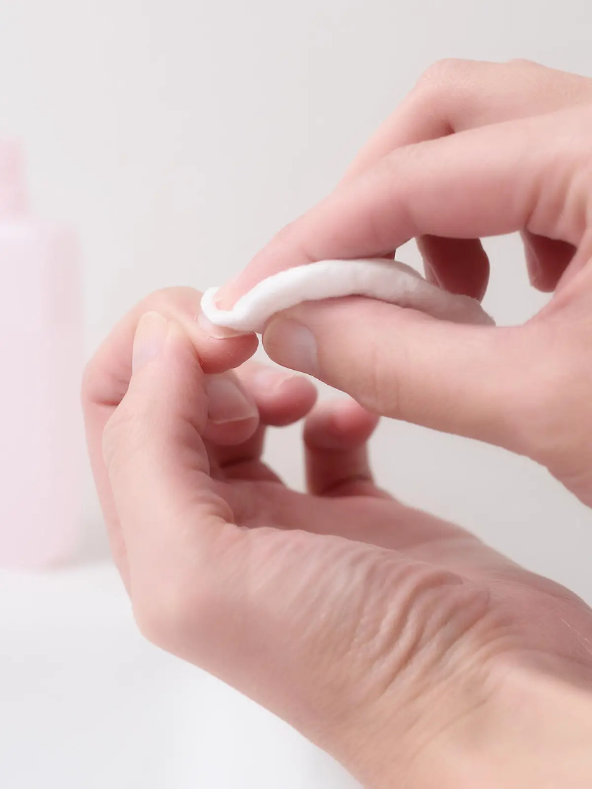 Woman removing nail varnish with acetone on a small cotton pad on the edge of a hand basin as she cares for her nails and cuticles in a health and beauty concept