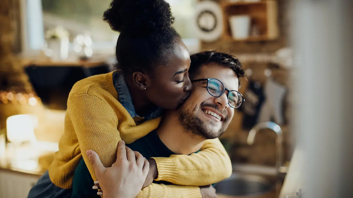 Young African American woman kissing her boyfriend having fun with him at home.