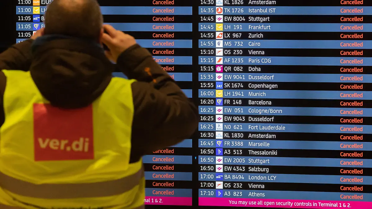 25.01.2023, Brandenburg, Schönefeld: Ein Mann mit Verdi-Weste fotografiert während eines Warnstreiks am Flughafen Berlin-Brandenburg BER eine Anzeigetafel, auf der alle Flüge als gestrichen angezeigt werden. Die Gewerkschaft Verdi hat zu einem ganztägigen Warnstreik am Flughafen Berlin-Brandenburg aufgerufen. Es werden voraussichtlich keine Passagierflüge abheben oder dort landen. Foto: Christoph Soeder/dpa +++ dpa-Bildfunk +++