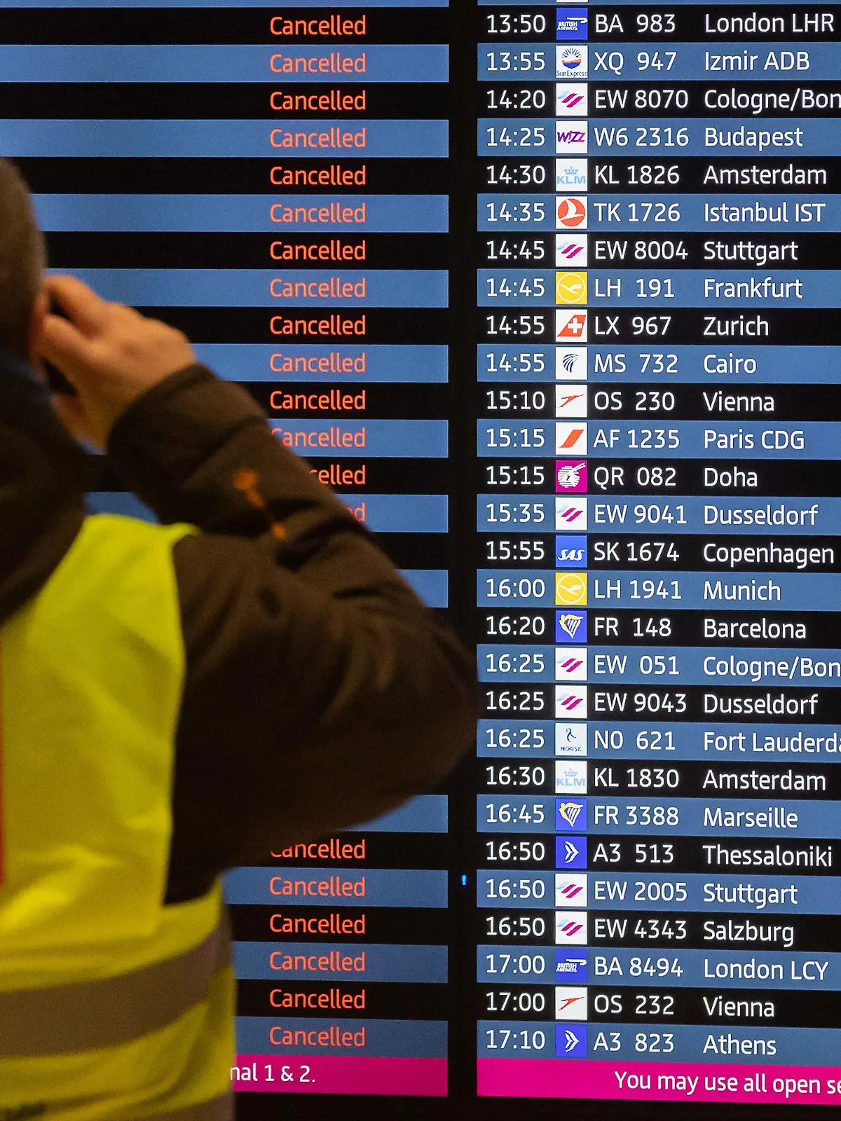 25.01.2023, Brandenburg, Schönefeld: Ein Mann mit Verdi-Weste fotografiert während eines Warnstreiks am Flughafen Berlin-Brandenburg BER eine Anzeigetafel, auf der alle Flüge als gestrichen angezeigt werden. Die Gewerkschaft Verdi hat zu einem ganztägigen Warnstreik am Flughafen Berlin-Brandenburg aufgerufen. Es werden voraussichtlich keine Passagierflüge abheben oder dort landen. Foto: Christoph Soeder/dpa +++ dpa-Bildfunk +++