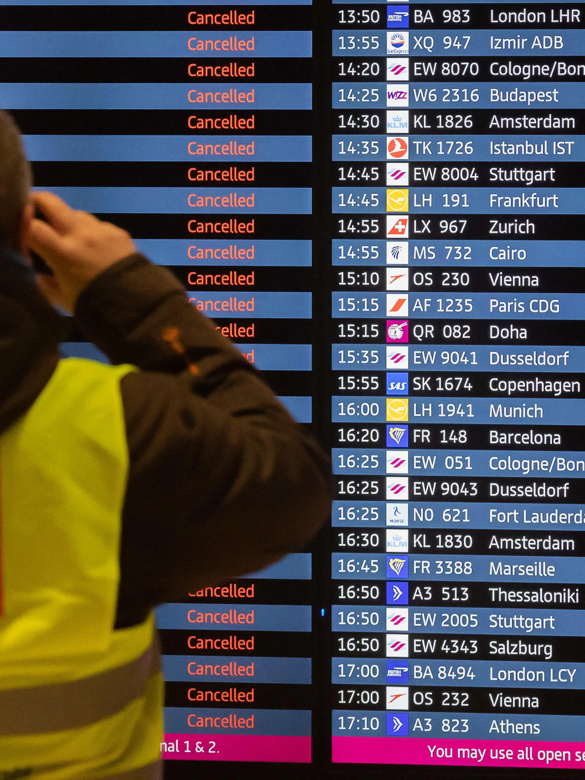 25.01.2023, Brandenburg, Schönefeld: Ein Mann mit Verdi-Weste fotografiert während eines Warnstreiks am Flughafen Berlin-Brandenburg BER eine Anzeigetafel, auf der alle Flüge als gestrichen angezeigt werden. Die Gewerkschaft Verdi hat zu einem ganztägigen Warnstreik am Flughafen Berlin-Brandenburg aufgerufen. Es werden voraussichtlich keine Passagierflüge abheben oder dort landen. Foto: Christoph Soeder/dpa +++ dpa-Bildfunk +++