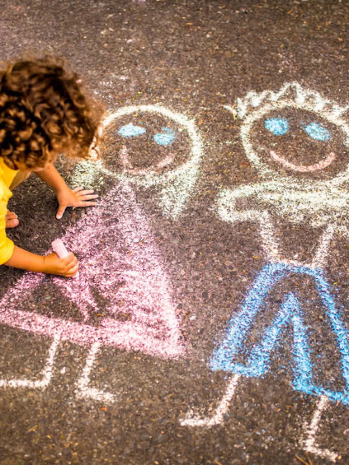 Overhead shot of a little boy drawing a  picture of his family in colourful chalk on tarmac