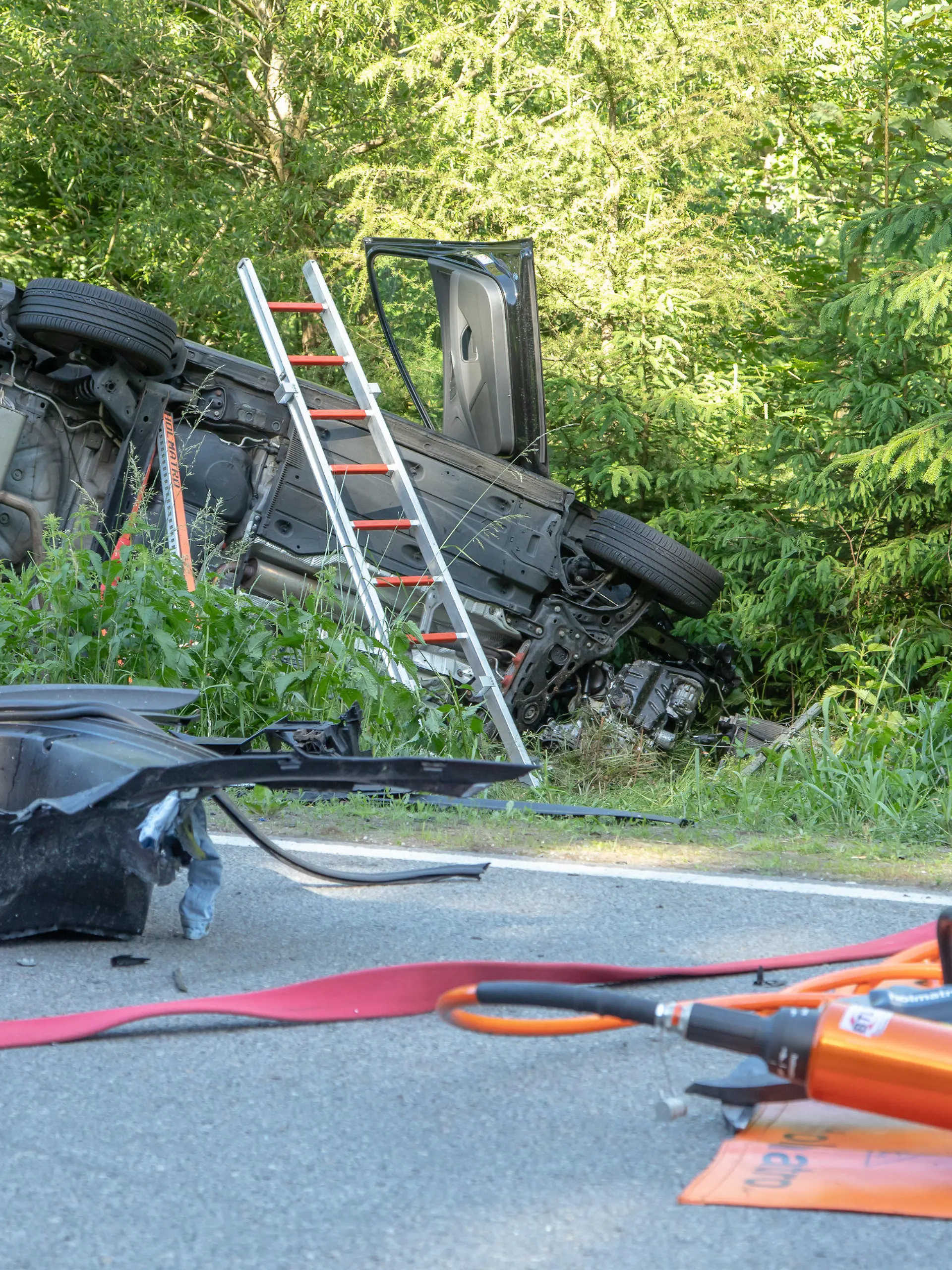 21.06.2020, Sachsen, Aue: Rettungswerkzeuge liegen neben einem Auto, das im Graben liegt. Beim Zusammenstoß von zwei Autos im Erzgebirgskreis sind am Sonntag drei Menschen gestorben. Eine Frau und zwei Kinder wurden verletzt, wie die Polizei Chemnitz mitteilte. Foto: Andre März/dpa-Zentralbild/dpa +++ dpa-Bildfunk +++