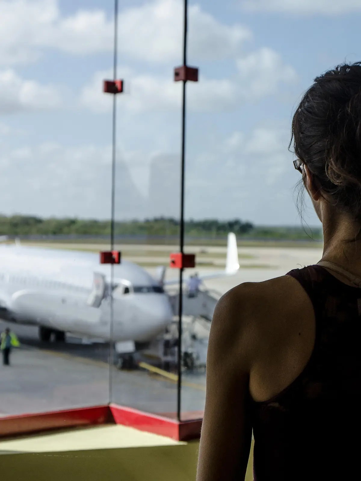 A woman, seen from behind, is looking at a plane from inside the airport