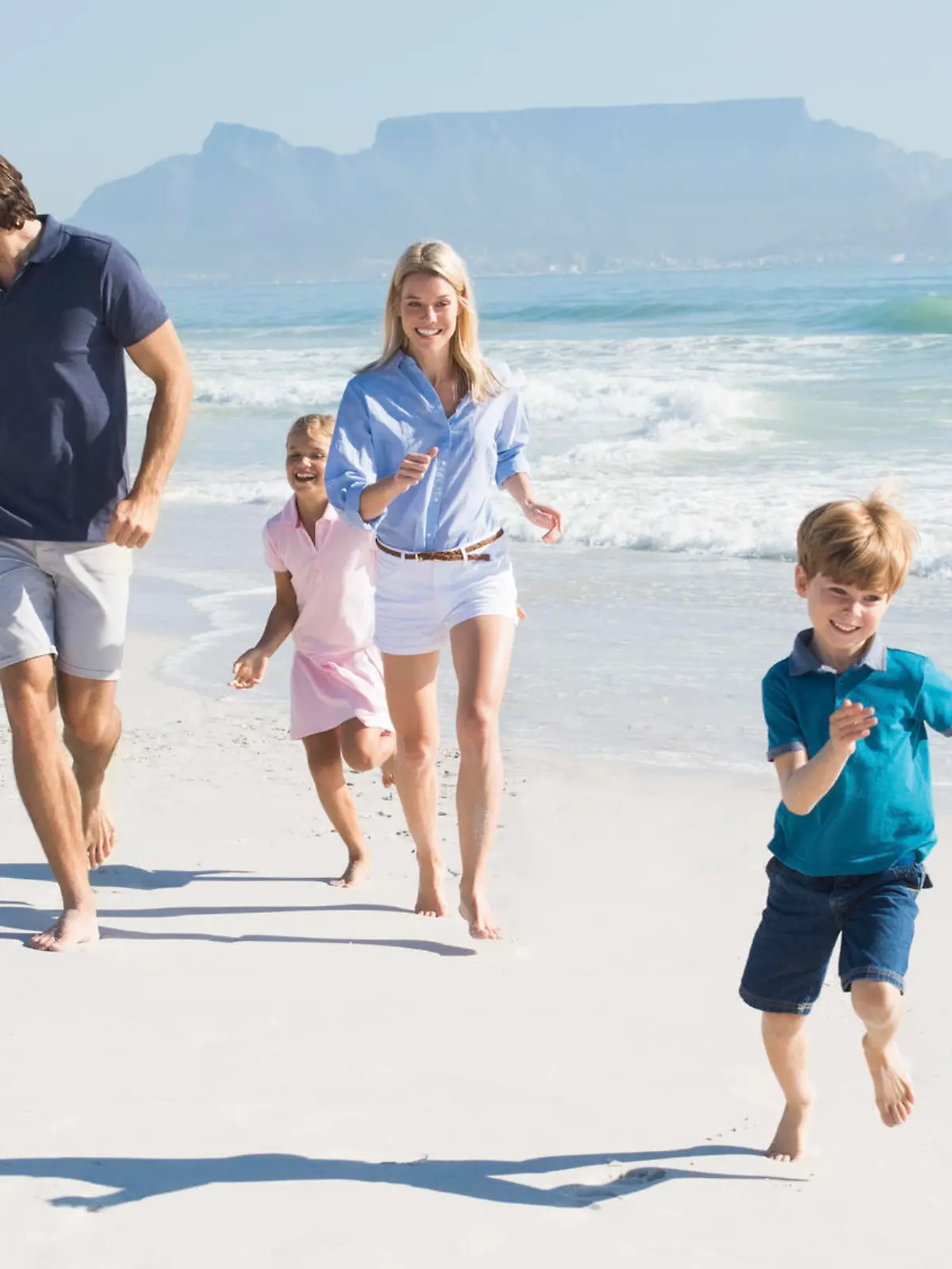 Family playing with pet on the beach. Happy beautiful family running at beach with pet dog. Smiling parents with son and daughter having fun at seaside.