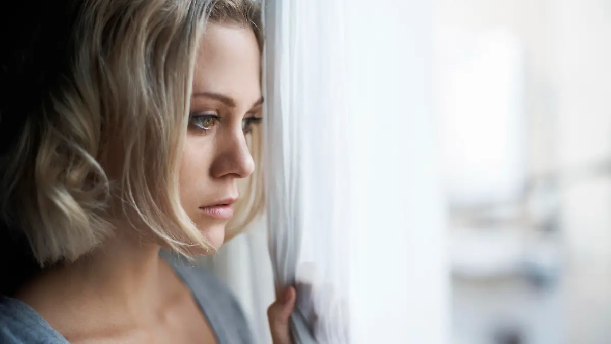 A beautiful young blonde woman looking out of her window sadly