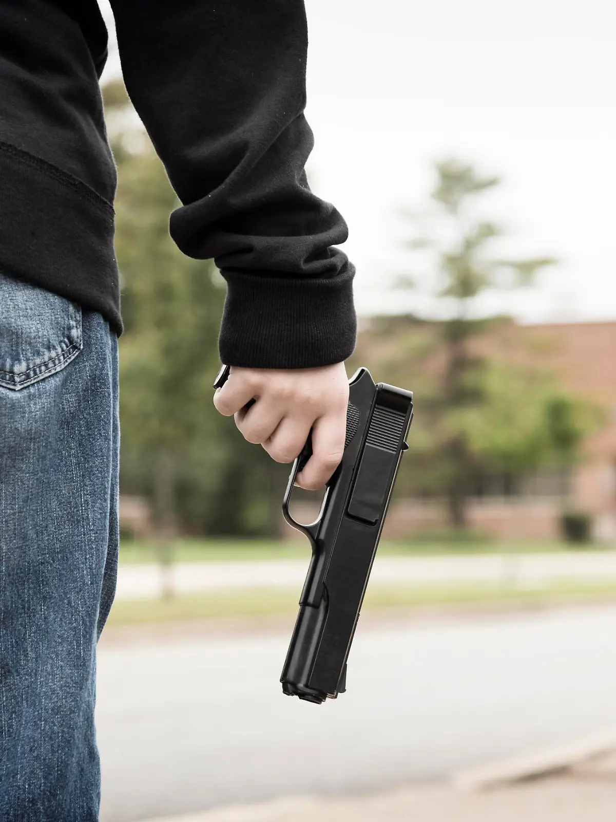A student wearing jeans and a black hoodie stands outside of school holding a gun.Similar Images: