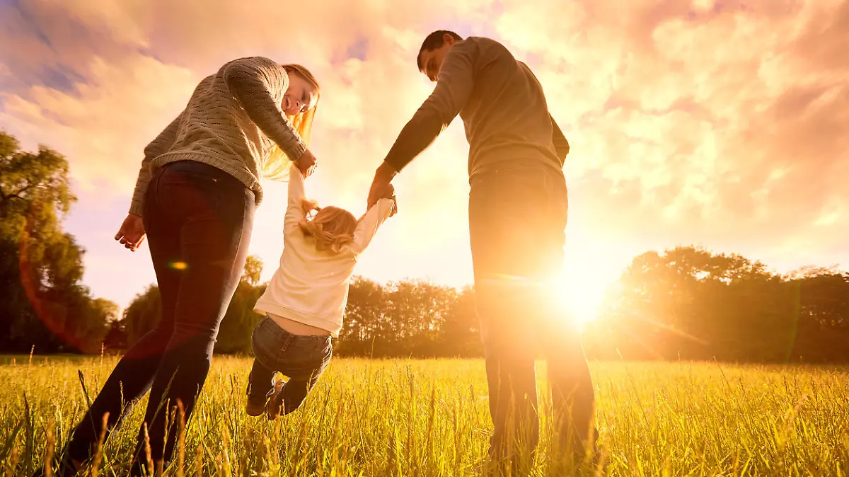 Happy family in the park evening light. The lights of a sun. Mom, dad and baby happy walk at sunset. The concept of a happy family.Parents hold the baby's hands.