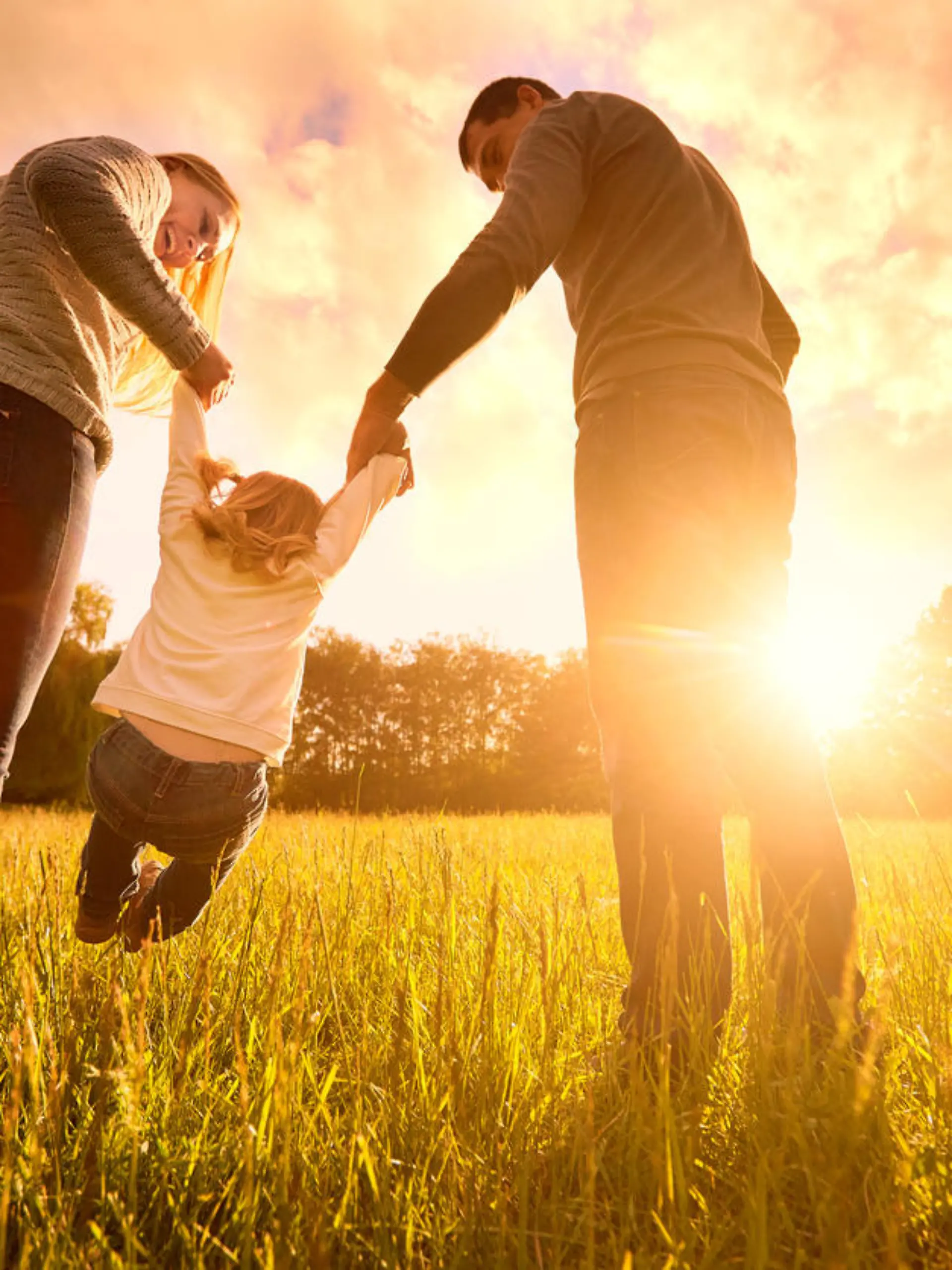 Happy family in the park evening light. The lights of a sun. Mom, dad and baby happy walk at sunset. The concept of a happy family.Parents hold the baby's hands.