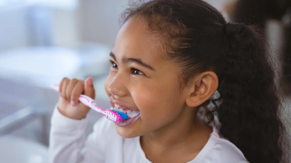 Cute biracial girl brushing teeth while looking away in bathroom. unaltered, childhood and hygiene concept. || Modellfreigabe vorhanden