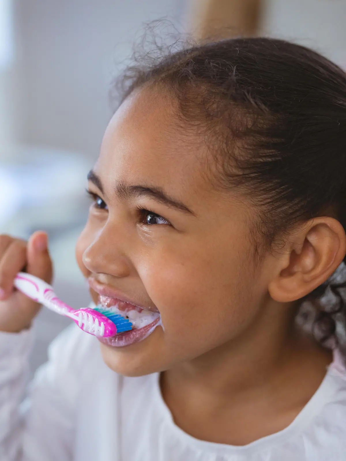 Cute biracial girl brushing teeth while looking away in bathroom. unaltered, childhood and hygiene concept. || Modellfreigabe vorhanden
