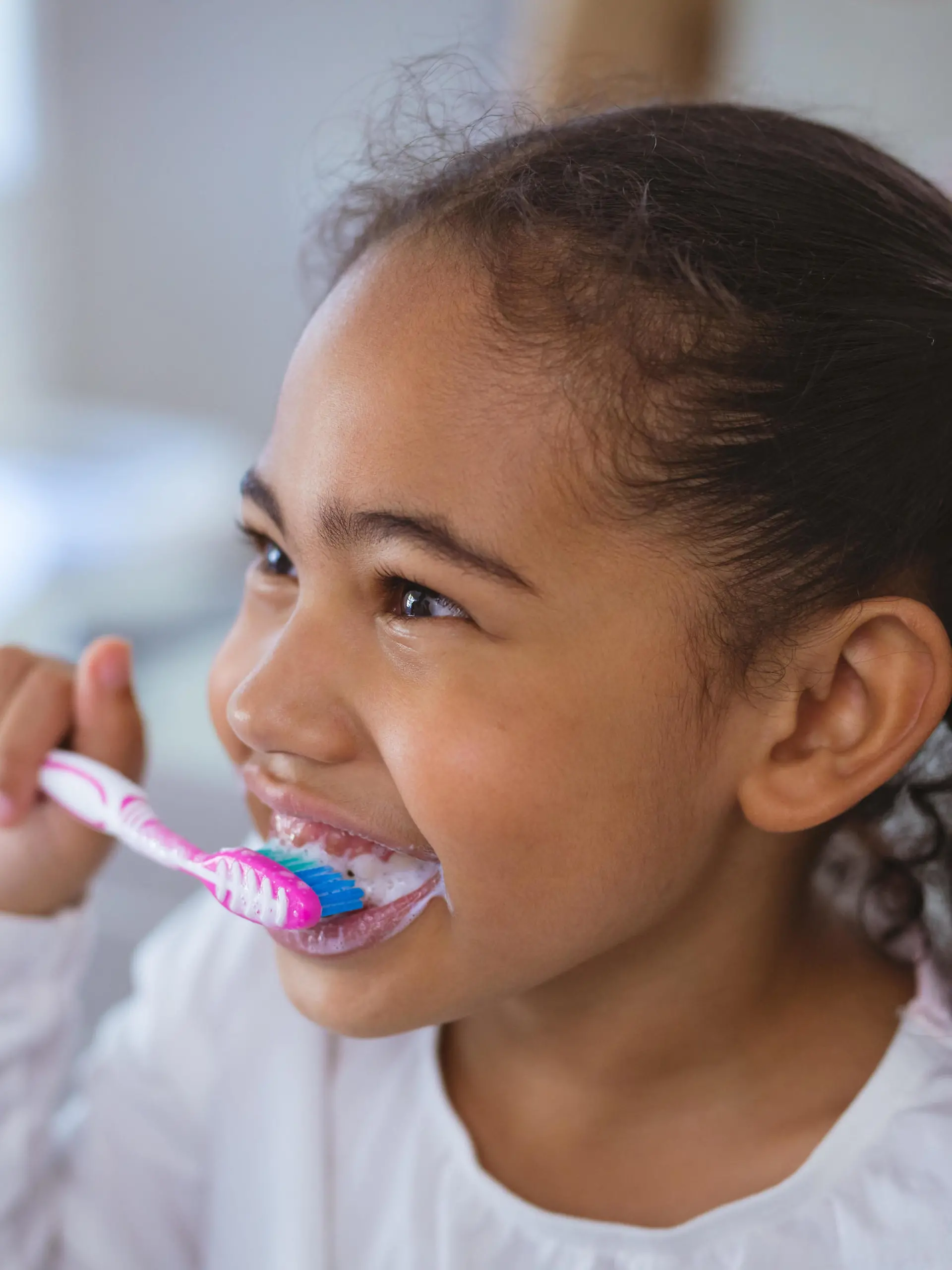 Cute biracial girl brushing teeth while looking away in bathroom. unaltered, childhood and hygiene concept. || Modellfreigabe vorhanden