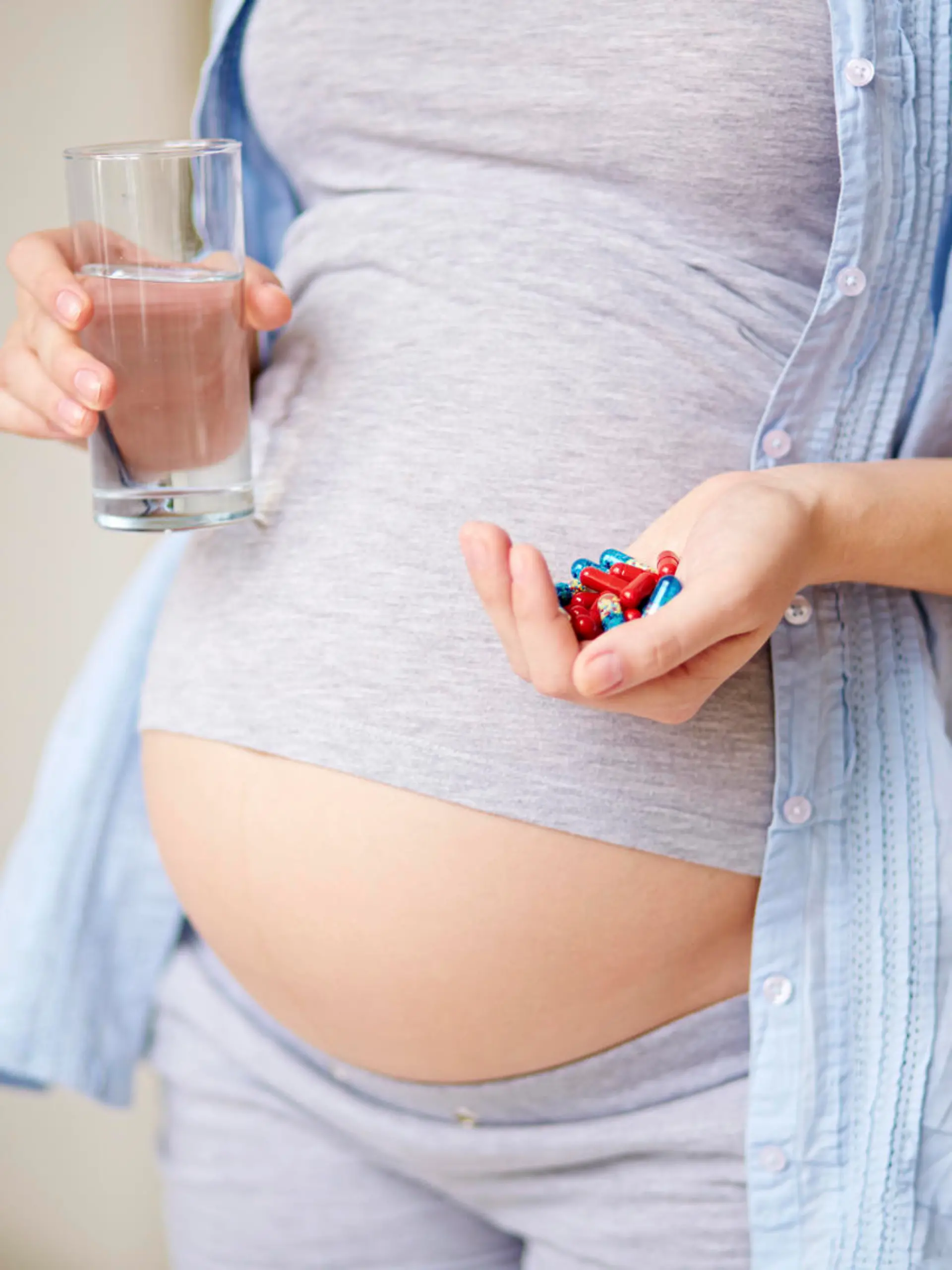 Mid section of pregnant woman holding glass of water and heap of pills
