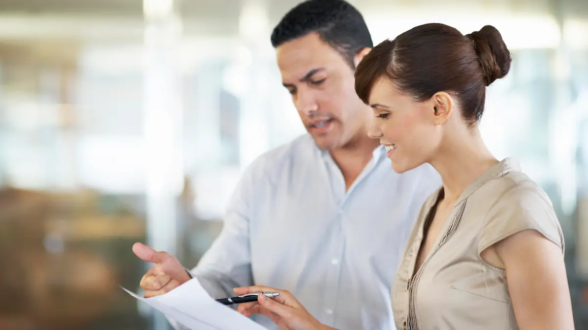 Shot of two coworkers standing in an office discussing paperwork