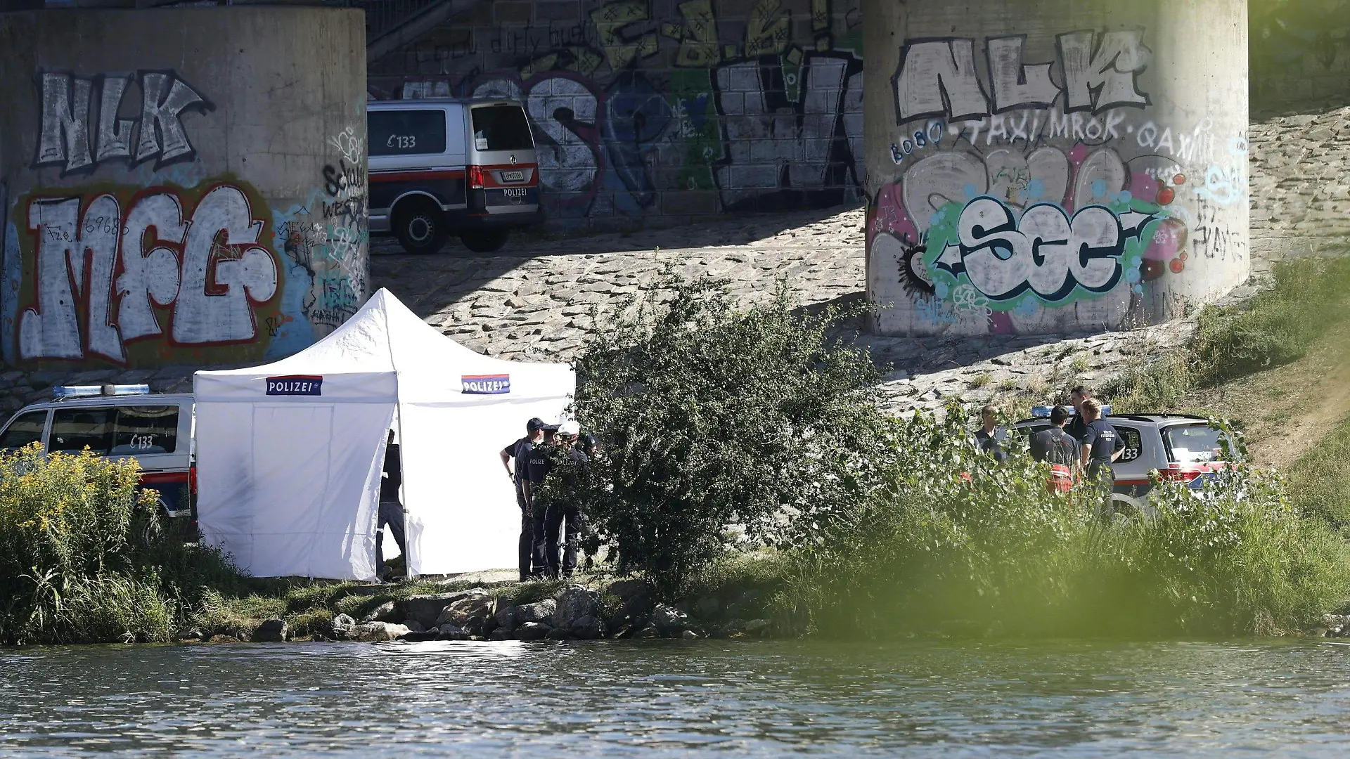 14.08.2023, Österreich, Wien: Einsatzkräfte ermitteln am Flussufer der Neuen Donau. Bei einer Hammerattacke wurde eine Frau verletzt - ihr vermisster fünfjähriger Sohn später tot in einem Seitenarm der Donau gefunden. Am Montag wurde dort eine weitere Leiche entdeckt. Foto: Tobias Steinmaurer/APA/dpa +++ dpa-Bildfunk +++