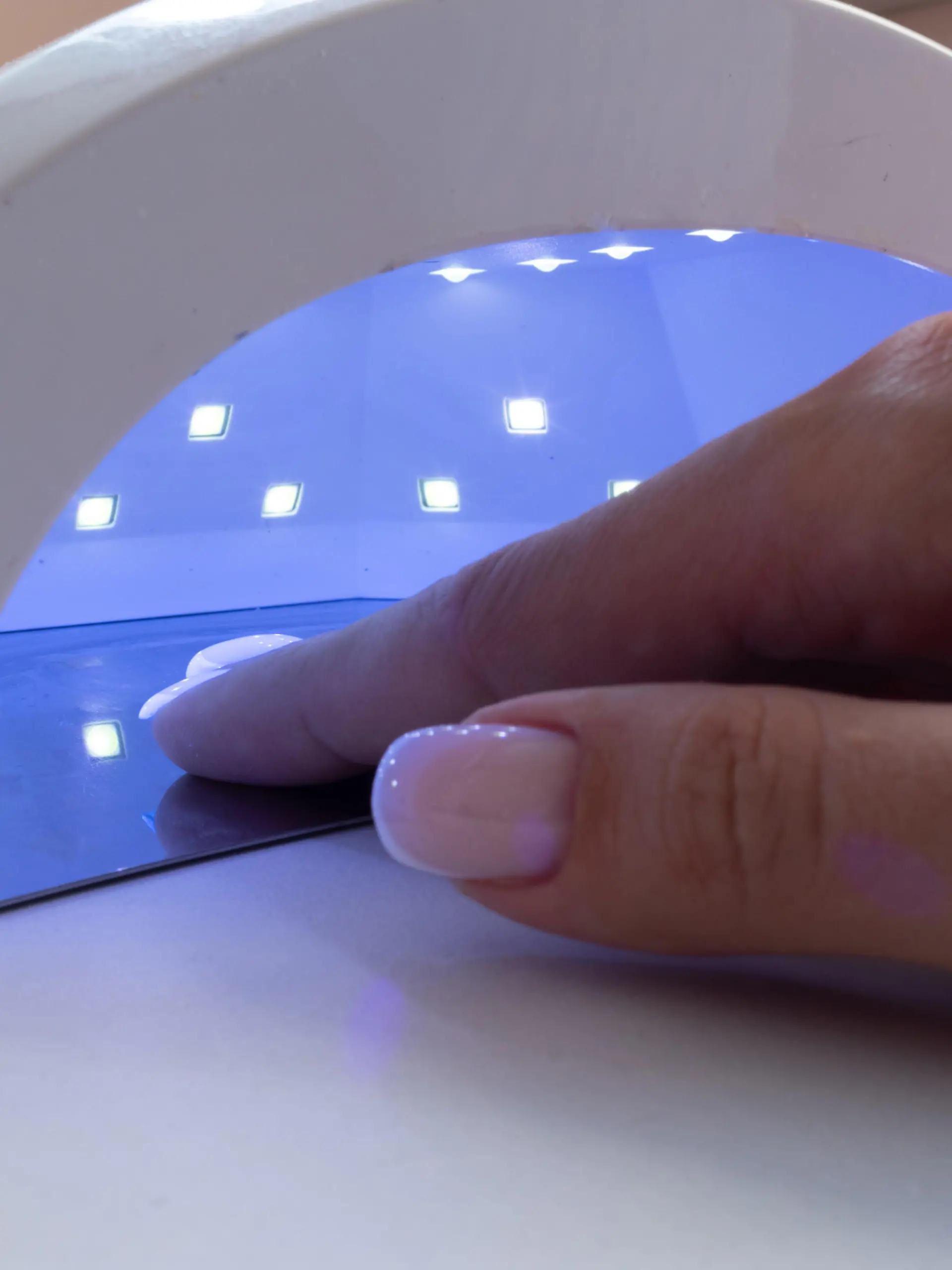 Female hand inside drying UV light machine in nail salon.