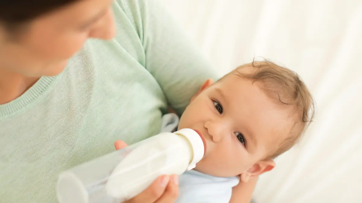 Mother feeding her baby boy with milk from a bottle.