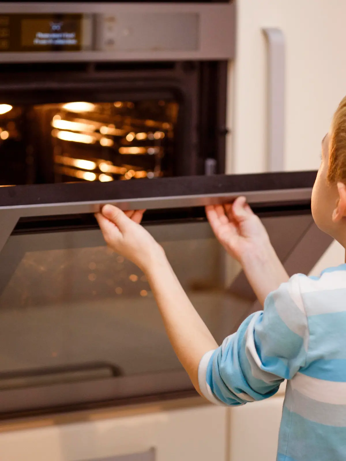Boy opening oven, baking cookies