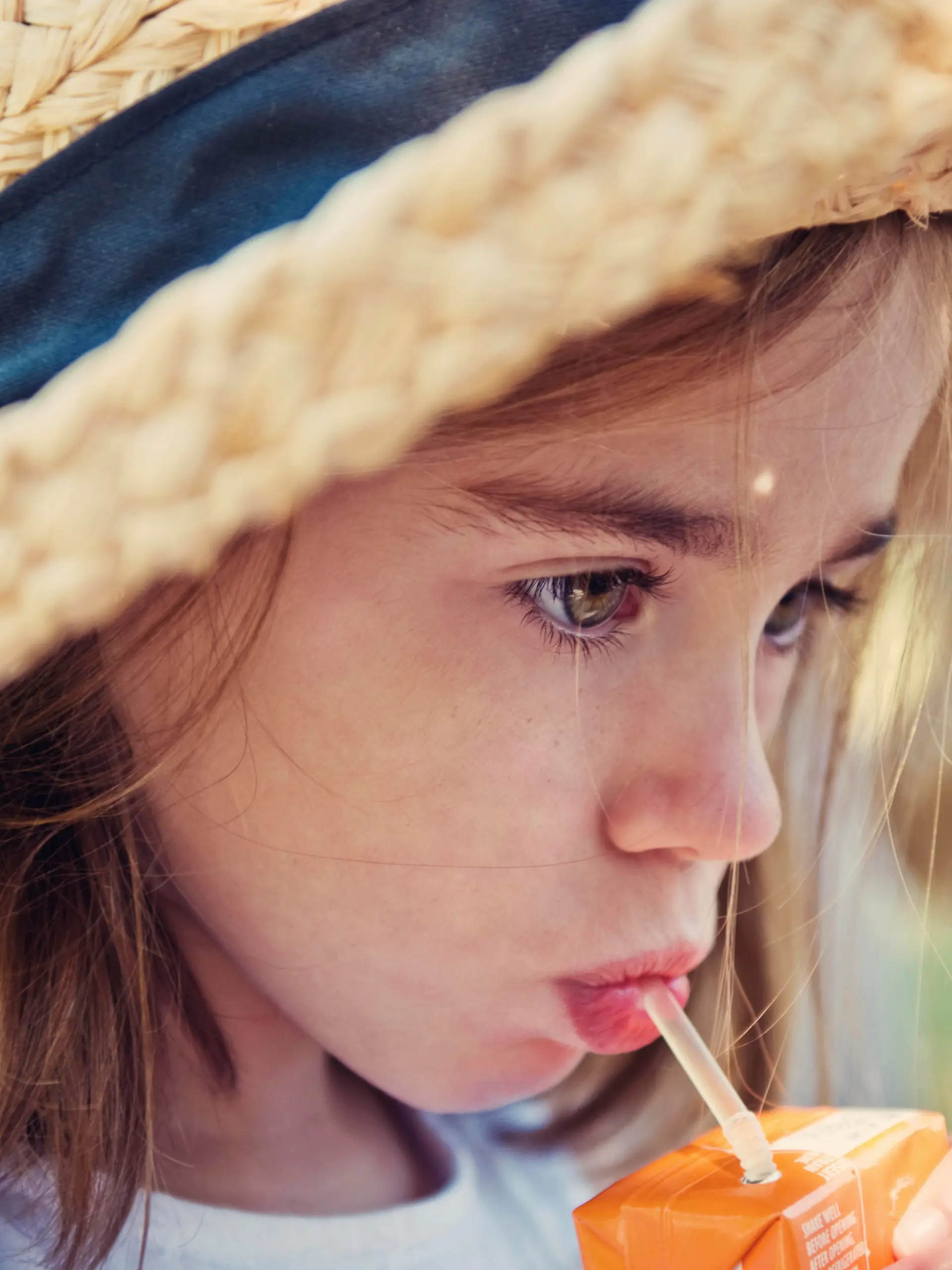 Little girl wearing straw hat and drinking from a juice box
