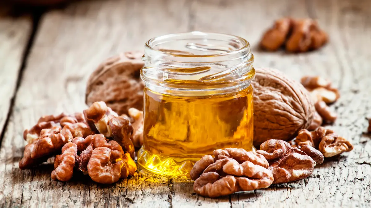 Walnut oil in a small jar and kernels on old wooden background in rustic style, selective focus
