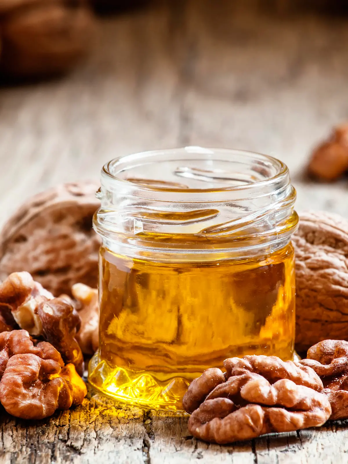 Walnut oil in a small jar and kernels on old wooden background in rustic style, selective focus