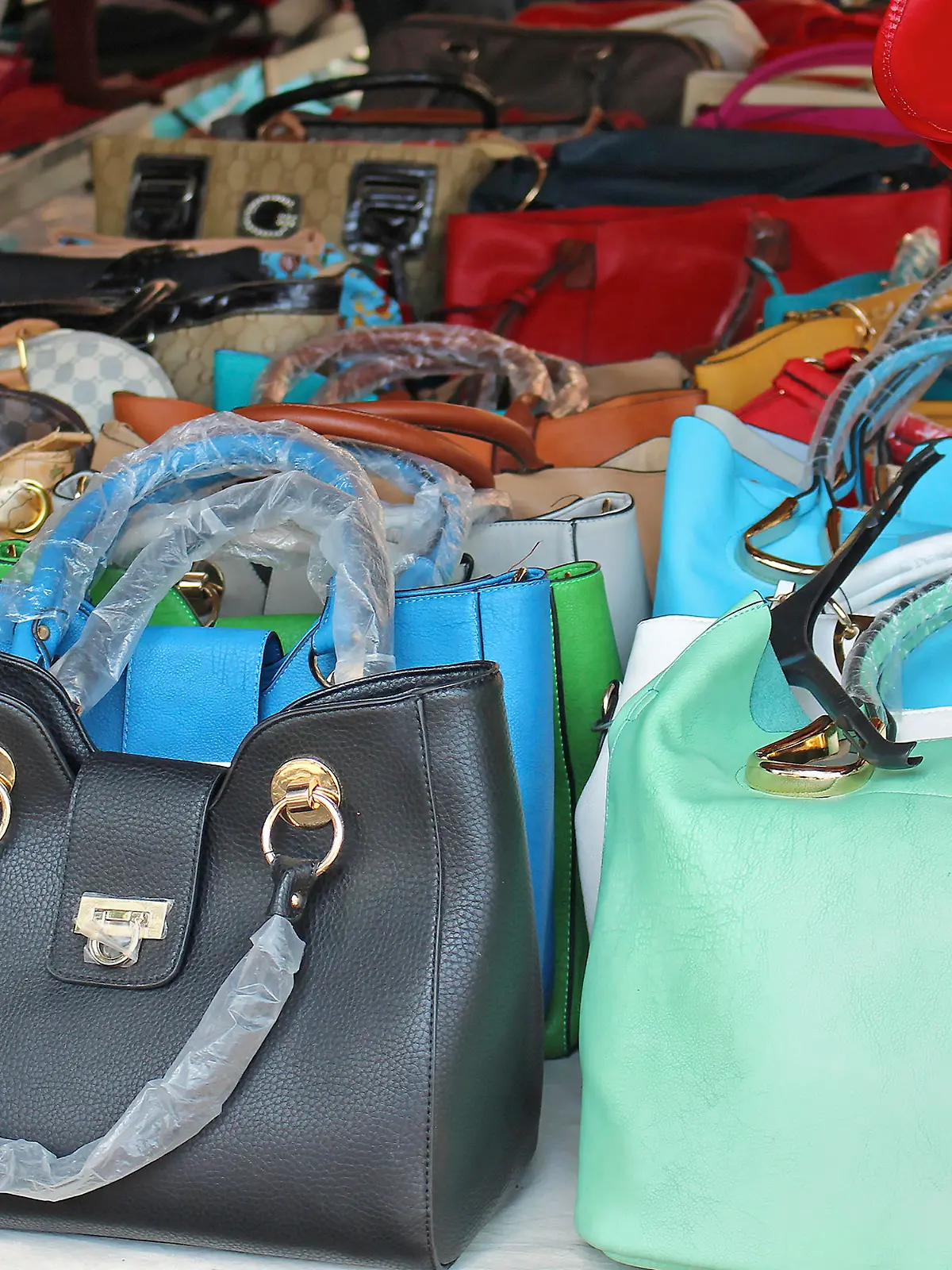 ROME, ITALY – JUNE 29, 2014: Big pile of colorful counterfeit handbags of famous fashion brands sold on Porta Portese flea market in Rome, Italy - June 29; Fake copies of popular fashion handbags