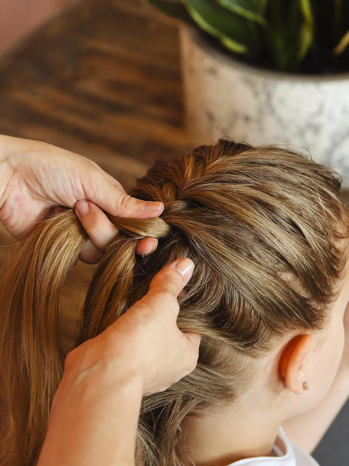 Young blonde girl getting her long hair braided by woman hairdresser before sport training while looking at cell phone with mockup screen and sitting on floor at home or fitness studio || Modellfreigabe vorhanden