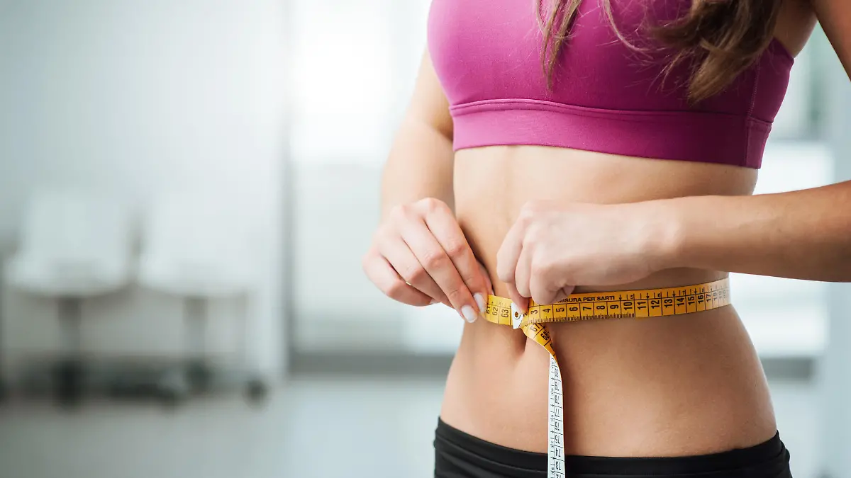 Frau misst ihre Taille mit Maßband.
