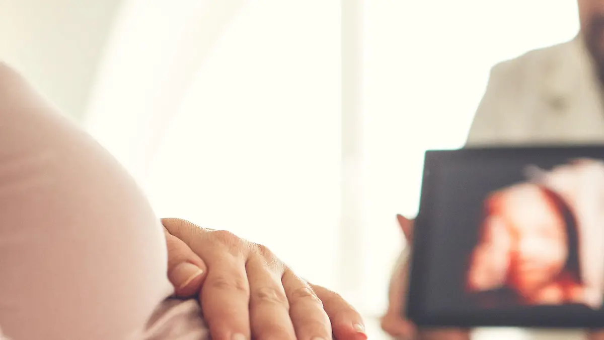 Pregnant woman looking at ultrasound image of her baby at doctor's office.