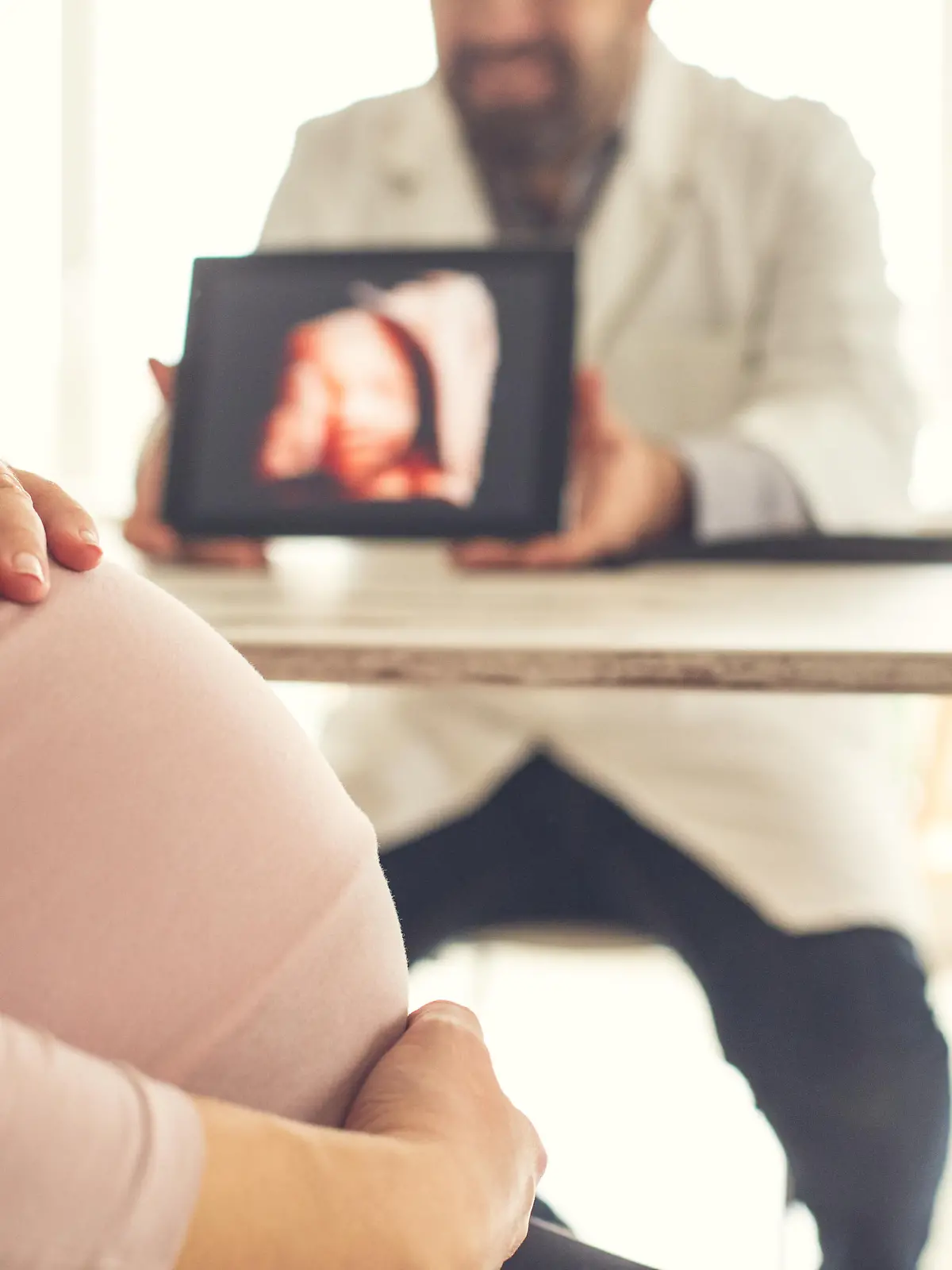 Pregnant woman looking at ultrasound image of her baby at doctor's office.