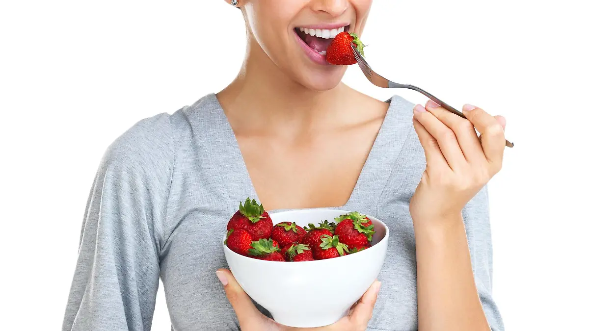 nette Brünette isst eine Schale Erdbeeren, lächelt in die Kamera