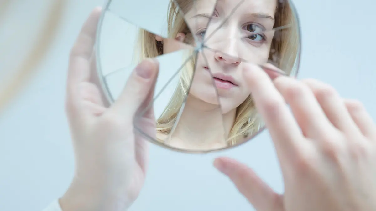 Insecure pretty young woman holding broken mirror