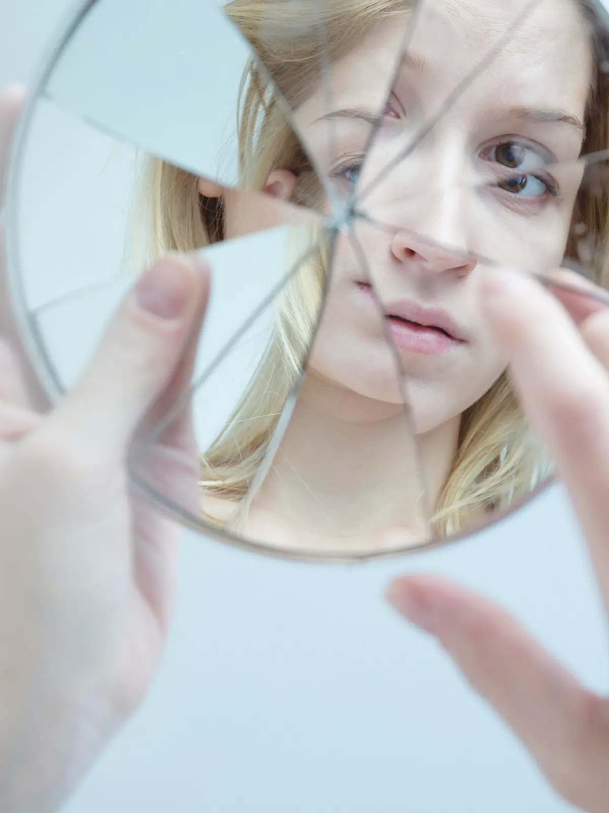 Insecure pretty young woman holding broken mirror