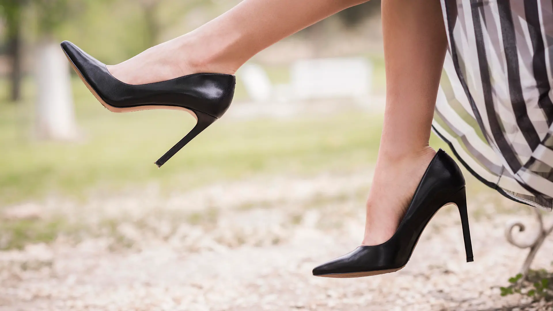Black high heels on the feet of a young woman in a park