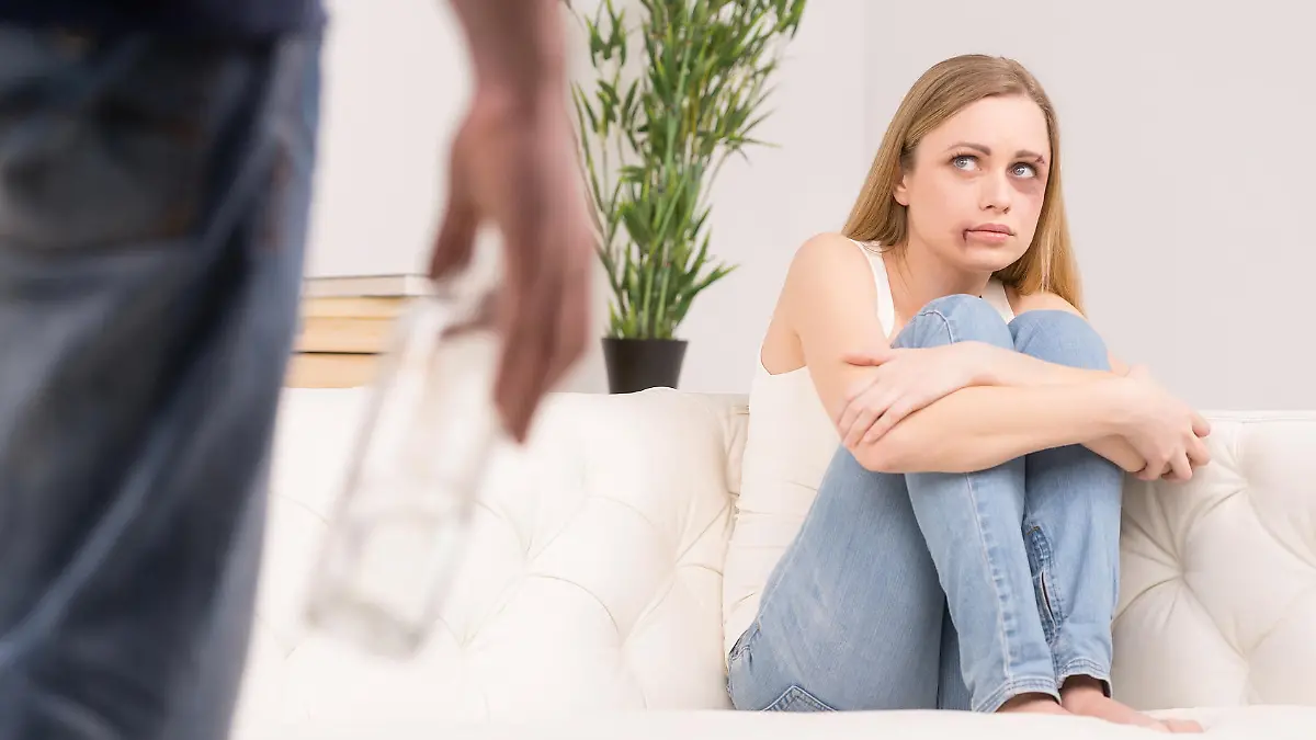 Scared woman is looking on drunk man on foreground. Having bruises on her pretty face 