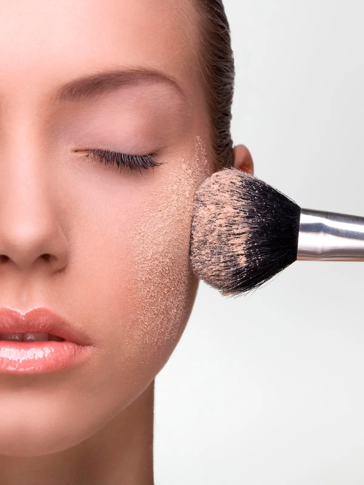 Young beautiful woman applying make-up powder on the cheek. Studio shot on neutral background.