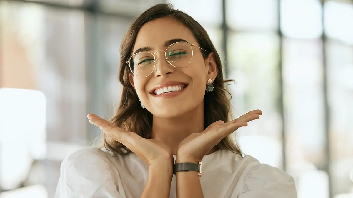 Cheerful business woman with glasses posing with her hands under her face showing her smile in an office. Playful hispanic female entrepreneur looking happy and excited at workplace