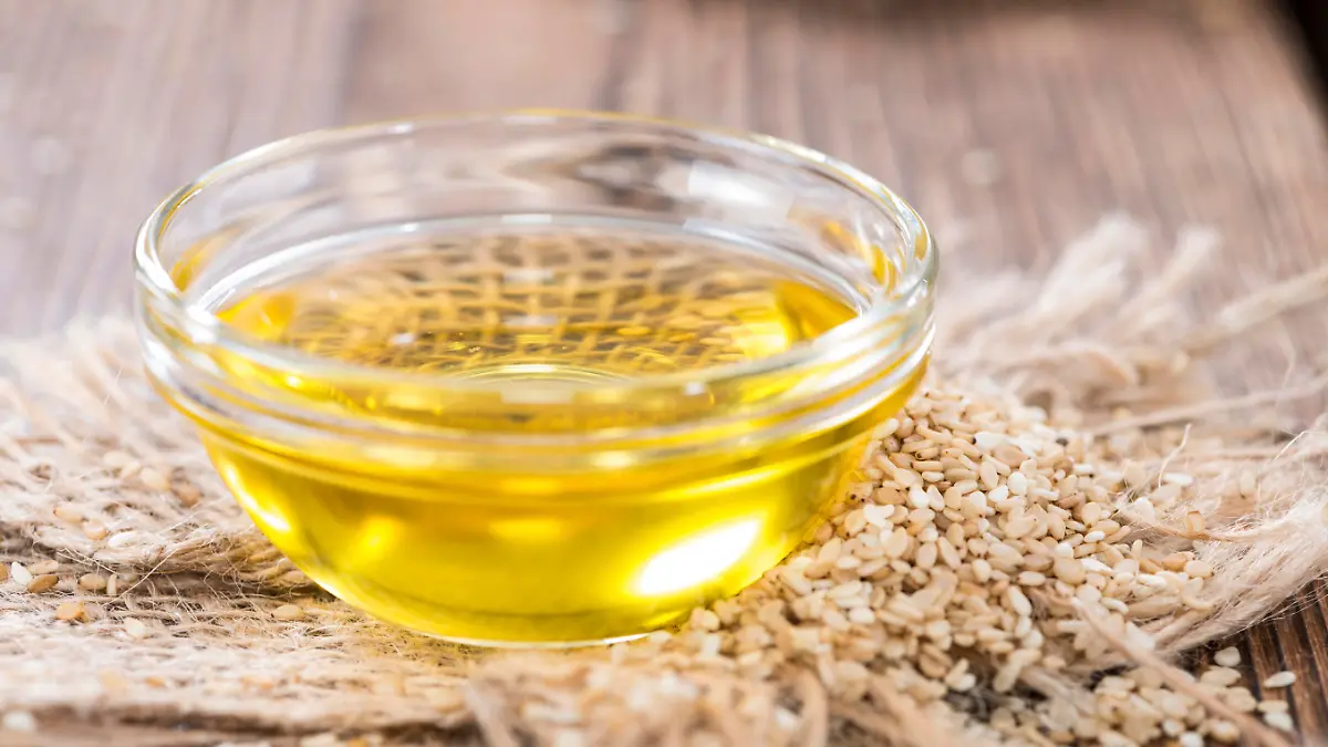 Sesame Oil with some Sesame Seeds on dark wooden table (close-up shot)