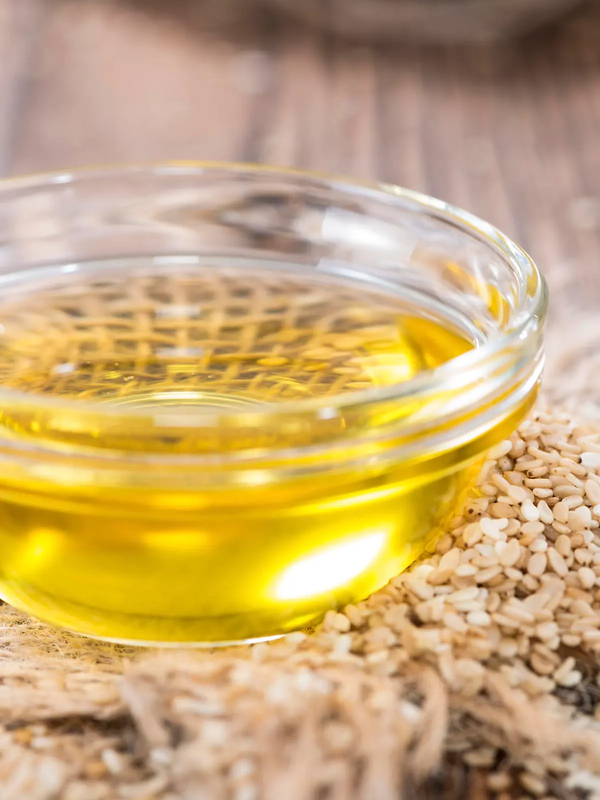 Sesame Oil with some Sesame Seeds on dark wooden table (close-up shot)