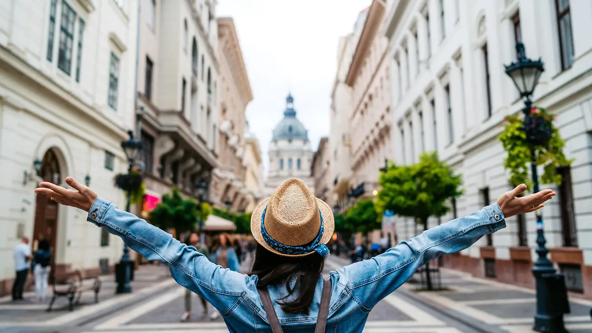 Young female tourist standing with outstretched arms on Budapest street, rear view.